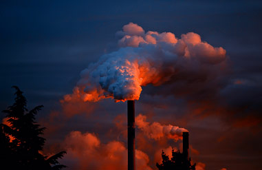 Two chimneys spewing pollution into the air at night