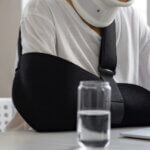 Woman wearing neck brace and arm sling working on a laptop