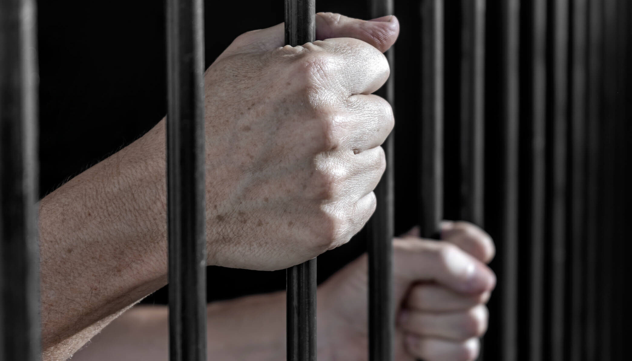 Prisoner's hands gripping the bars of a cell in jail.